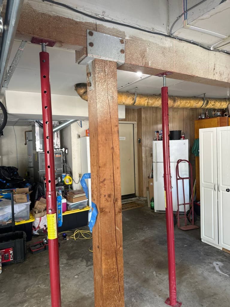 Dangerous vertical split in load-bearing timber post held safely by temporary red shoring jacks