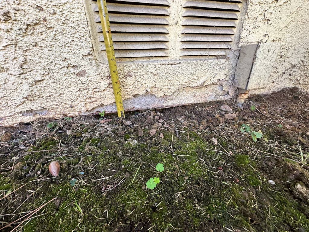Lack of foundation clearance with stucco embedded directly into saturated soil and moss growth