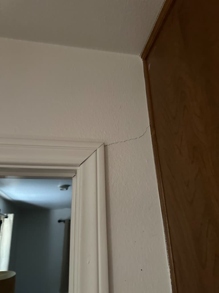 Interior drywall hairline shear crack propagating from door casing corner due to foundation deflection